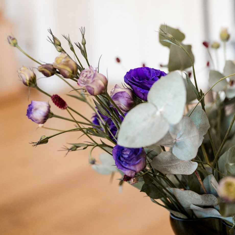 Nahaufnahme eines Blumenstraußes mit lila Blüten und silbergrünen Eukalyptusblättern in einer dunklen Vase.